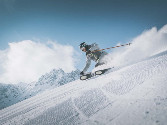 Skifahren in Ladurns Skifahrer fährt mit hoher Geschwindigkeit die Piste hinunter bei klarem Himmel