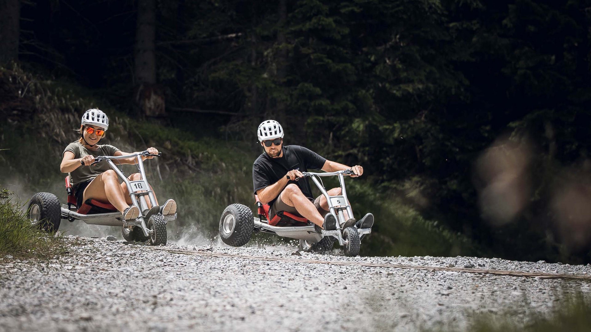 I nostri alloggi a Colle Isarco: una base per mille avventure Due persone guidano mountain cart su un sentiero sterrato nella foresta