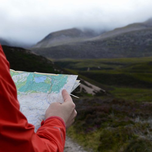 Aktivhotel in Südtirol: Sommererlebnisse Person in roter Jacke liest Karte vor nebligen Bergen