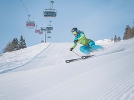 Skifahren in Ladurns Skifahrer in grüner Jacke fährt auf frisch präparierter Piste bei klarem Himmel
