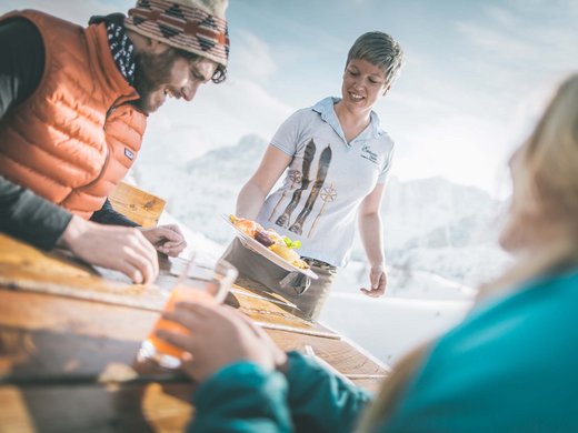 Skifahren in Ladurns Kellnerin serviert Gästen Essen an Holztisch in verschneiter Berglandschaft