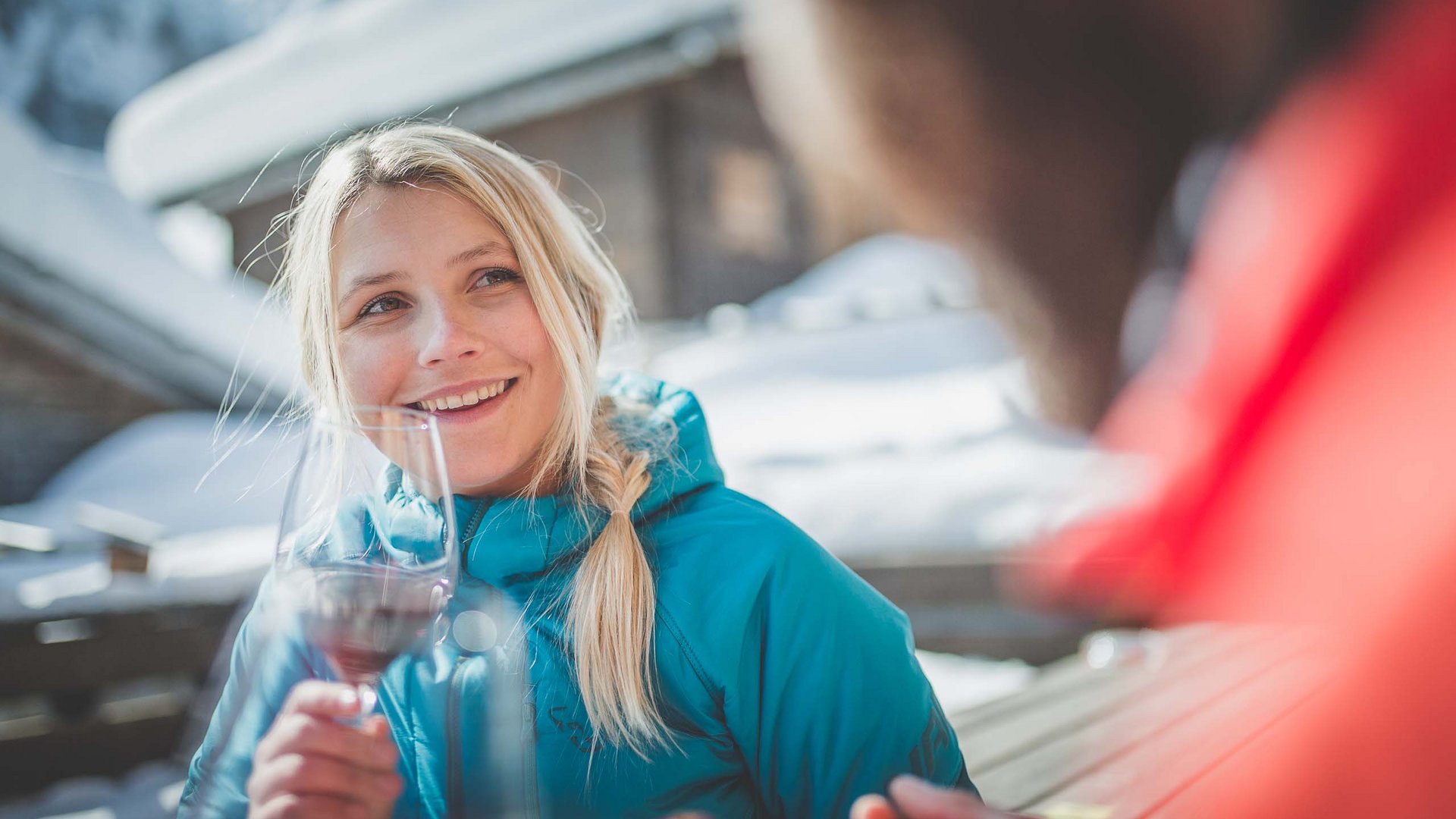 Frau in blauer Jacke trinkt Wein und lächelt im verschneiten Winter