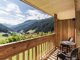 Familienhotel in Südtirol: Hotel Panorama Balkon mit Holzgeländer und Tisch mit zwei Stühlen in den Bergen bei Sonnenschein