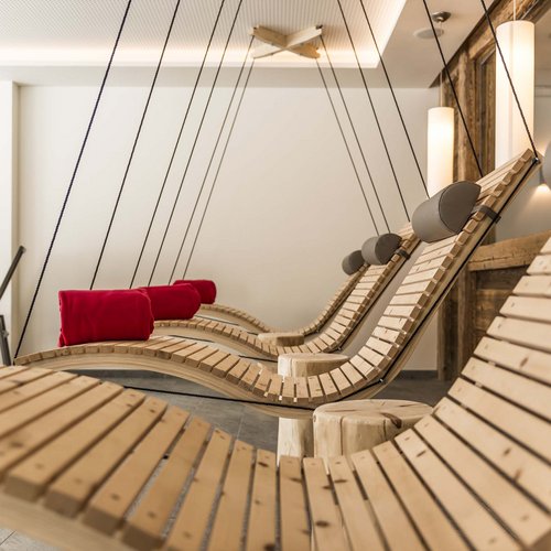 Wellness in der Unterkunft im Pflerschtal Hängende Holzliegen mit roten Kissen in einem modernen Ruheraum