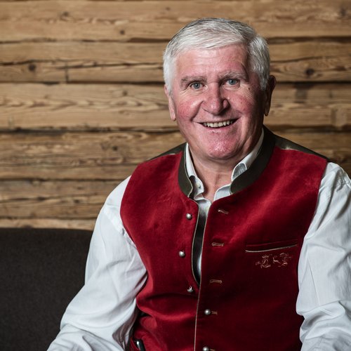 Familienhotel in Südtirol: Hotel Panorama Älterer Mann in roter Trachtenweste vor Holzwand