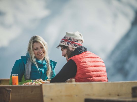 Skifahren in Ladurns Paar in Winterkleidung isst im Freien vor schneebedeckten Bergen