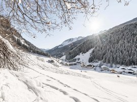 Familienhotel in Südtirol: Hotel Panorama Verschneites Dorf in einem Tal umgeben von Bergen unter strahlendem Sonnenschein