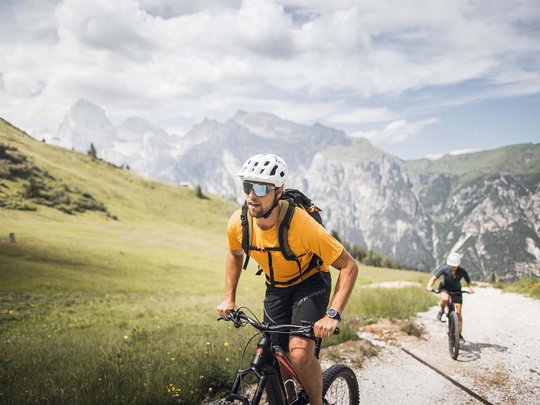 Lo sport a Colle Isarco vi coinvolgerà Due ciclisti con casco pedalano su sentiero montano in paesaggio verde
