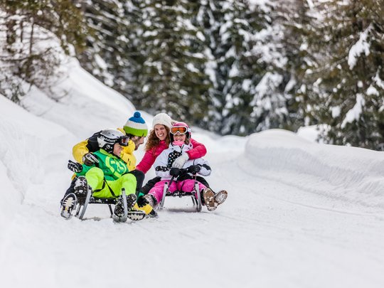Pflerschtal: Skigebiet, Wandergebiet und mehr Familie fährt Schlitten auf schneebedeckter Winterstrecke mit Tannenbäumen