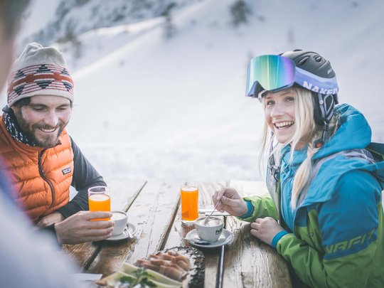 Vacanze invernali in Val di Fleres Due persone bevono caffè e succo a un tavolo in legno all'aperto sulla neve