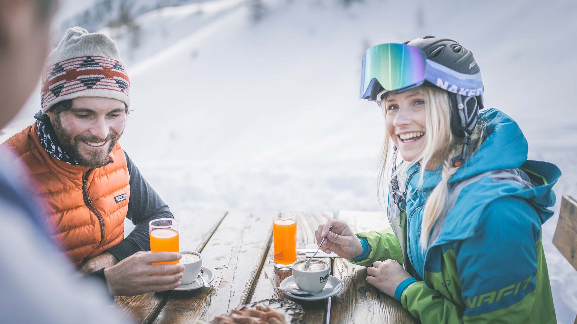 A Ladurns, c’è l’hotel perfetto per le vacanze invernali Due persone bevono caffè e succo a un tavolo in legno all'aperto sulla neve