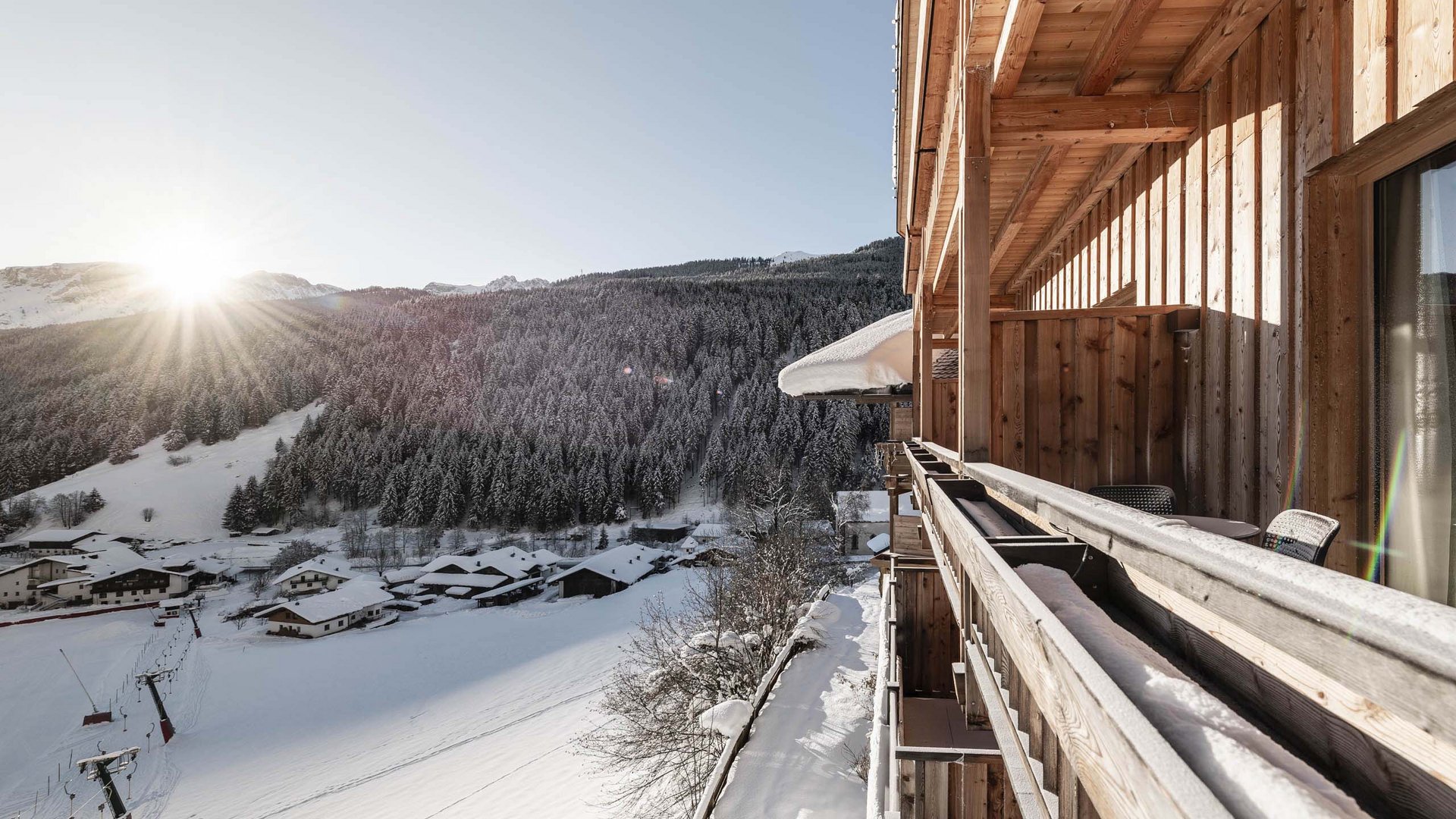 Balkon eines Holzchalet mit Blick auf verschneite Berge und Sonnenaufgang