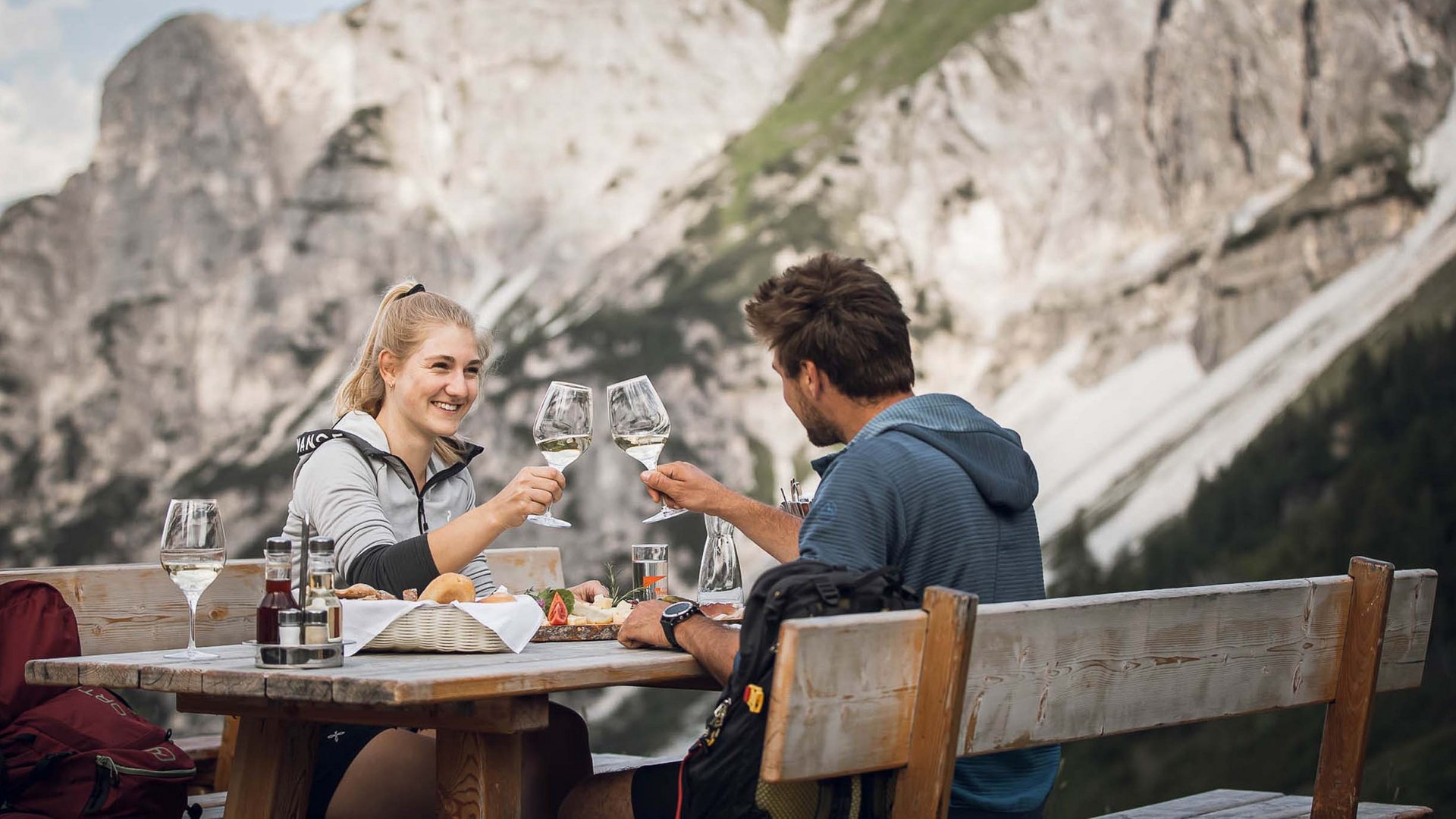 Aktivhotel in Südtirol: Sommererlebnisse Paar stößt mit Wein vor Berglandschaft bei Holztisch an