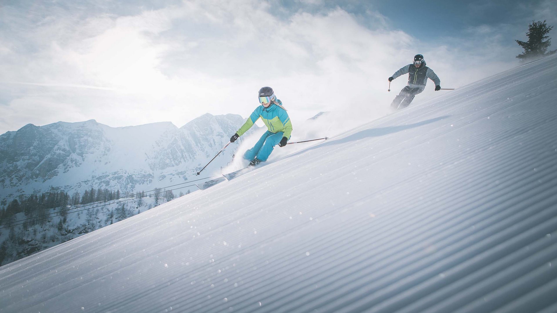 A Ladurns, c’è l’hotel perfetto per le vacanze invernali Due sciatori che scendono velocemente una pista innevata con montagne sullo sfondo