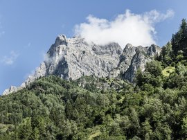 Familienhotel in Südtirol: Hotel Panorama Felsiger Berg mit grünen Bäumen und Wolke am blauen Himmel