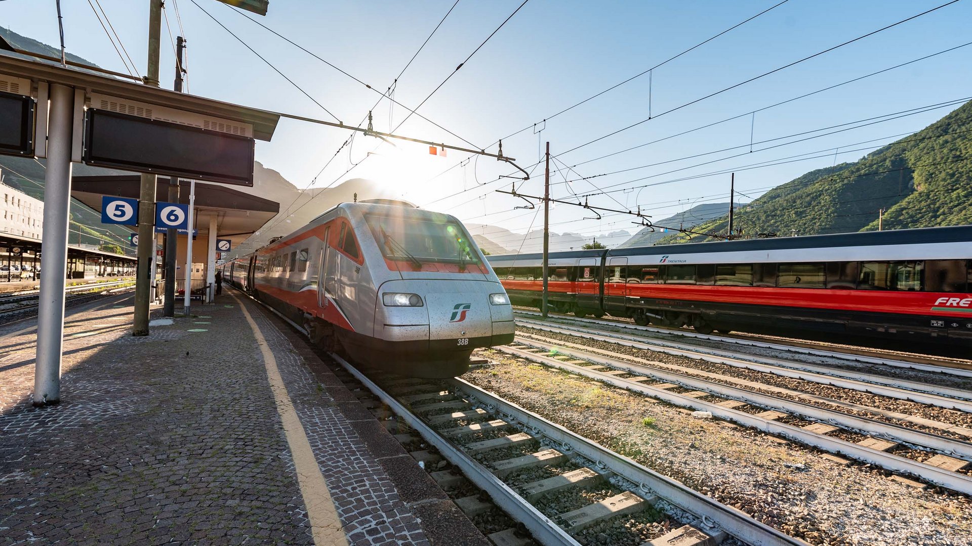 Passenger train at a sunny station with mountains in the background