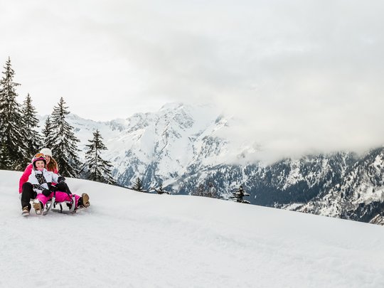 Pflerschtal: Skigebiet, Wandergebiet und mehr Zwei Personen rodeln auf einer verschneiten Bergpiste mit bewölkten Gipfeln