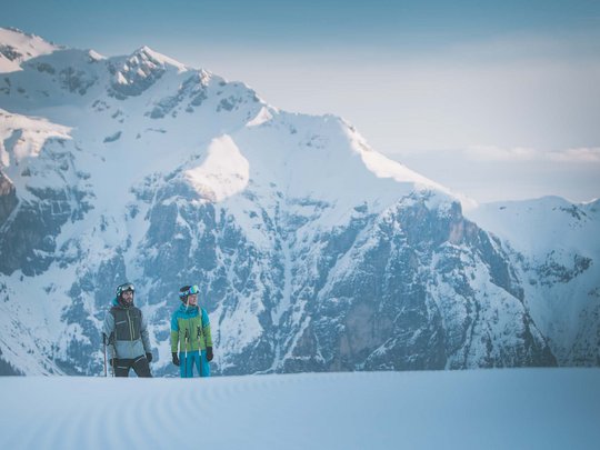 Skifahren in Ladurns Zwei Skifahrer stehen auf einer schneebedeckten Fläche vor verschneiten Bergen