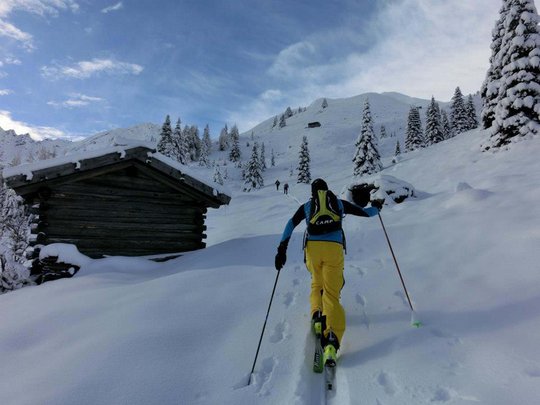 Ski touring in Pflerschtal Skier in yellow pants hiking through snowy winter landscape near wooden hut
