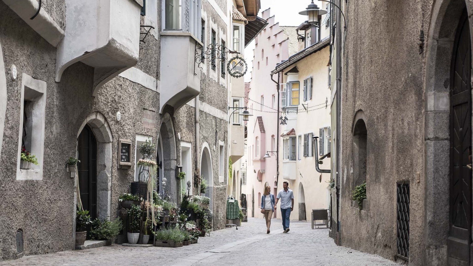 Hotel Panorama in Gossensass – Unterkunft zum Träumen Paar geht durch eine enge, historische Gasse mit alten Häusern und Blumen