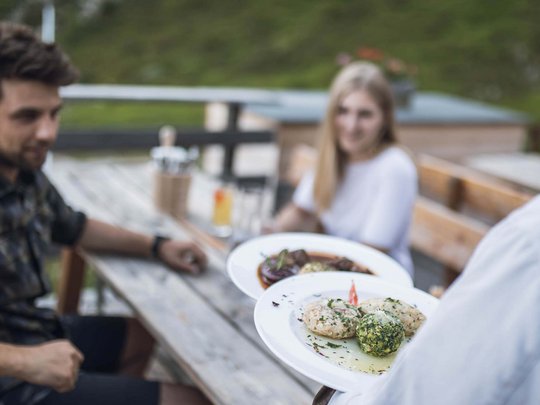 Aktivhotel Panorama: Wandern Kellner serviert Essen an Outdoor-Holztisch mit zwei Gästen