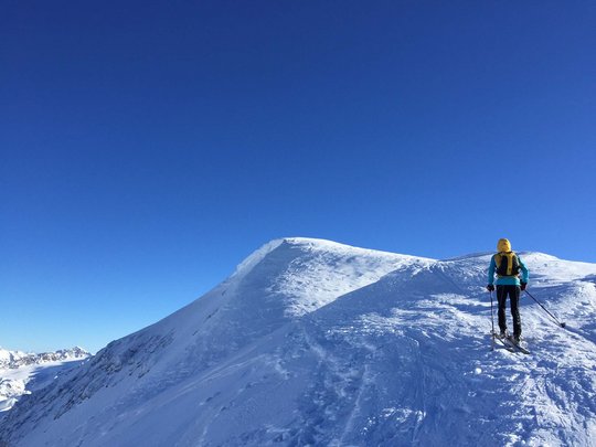 Ski touring in Pflerschtal Skier in yellow jacket on snowy mountain with clear blue sky