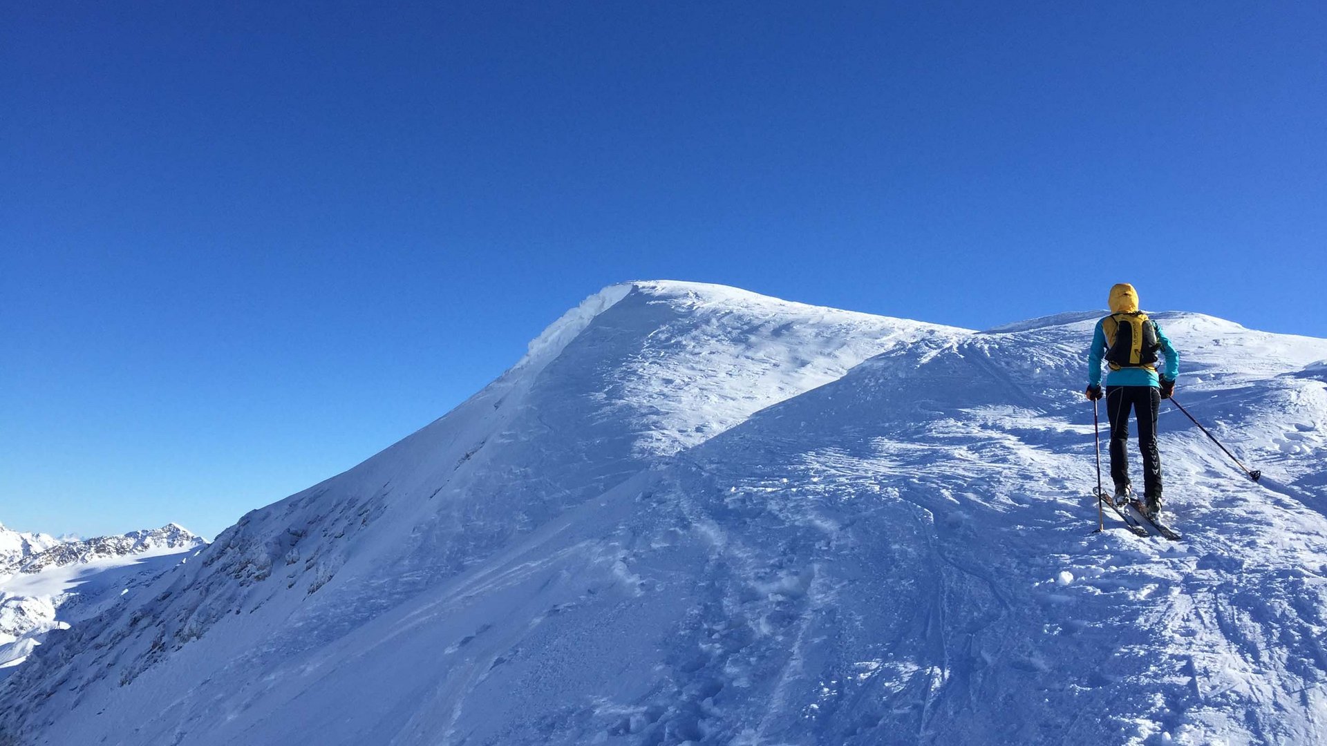 Sciatore con giacca gialla sulla montagna innevata sotto un cielo blu limpido