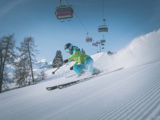 A Ladurns, c’è l’hotel perfetto per le vacanze invernali Sciatrice con giacca verde scende velocemente su pista innevata con seggiovia