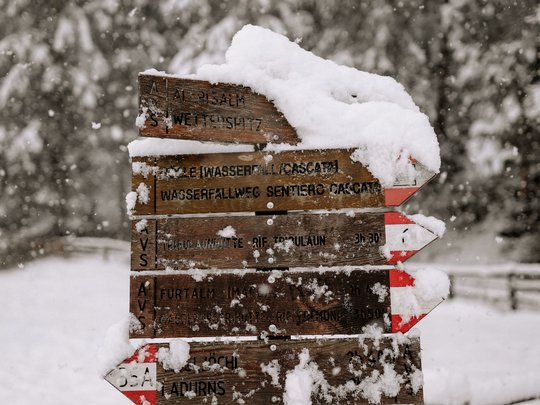 Family hotel vicino a Vipiteno: “hallo” e benvenuti! Segnaletica in legno coperta di neve in una foresta durante una nevicata
