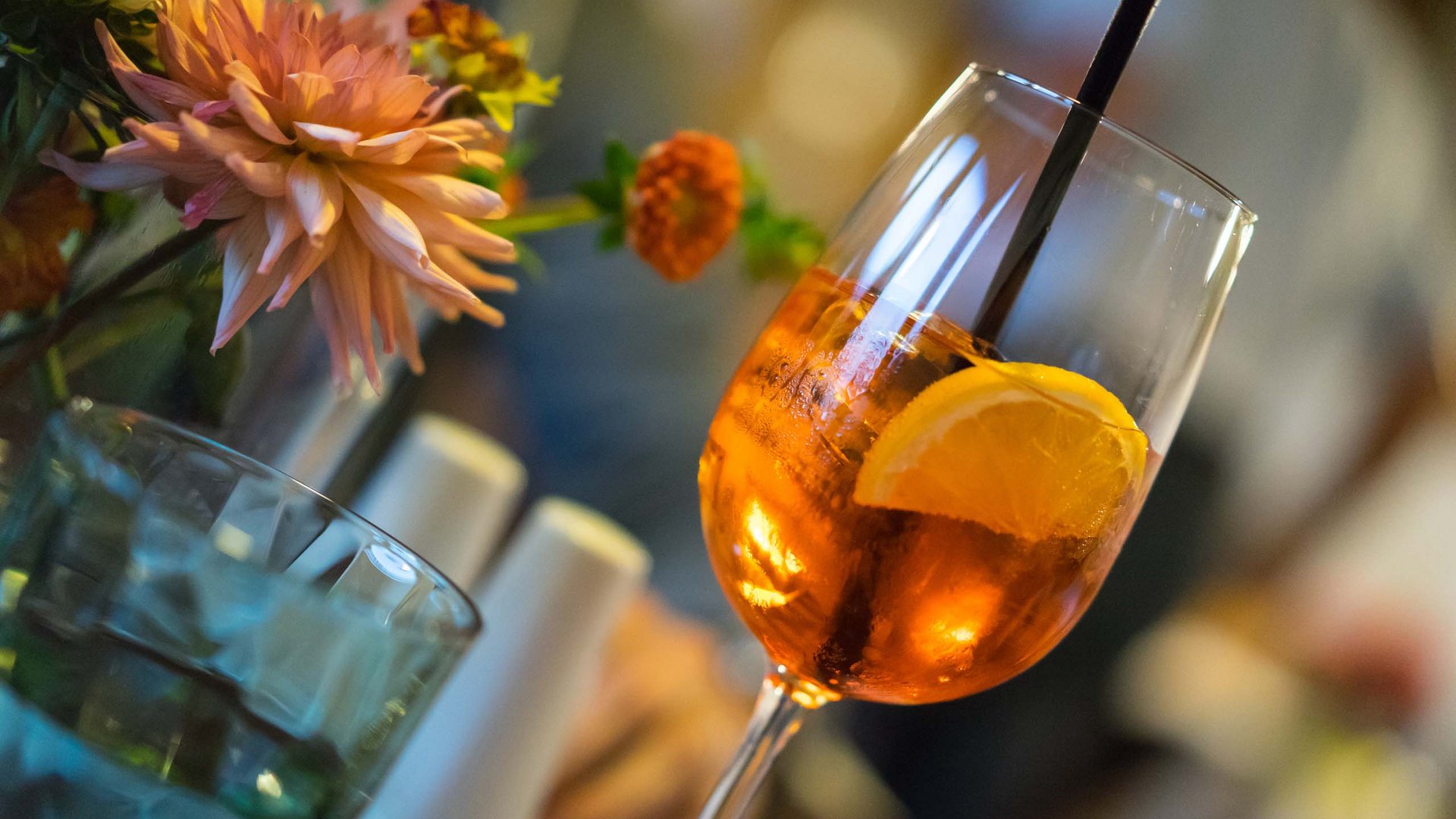 Genuss aus Pflersch: Hotel Panorama Cocktailglas mit Orangenscheibe und Strauß bunter Blumen im Hintergrund