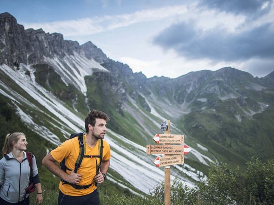 Aktivhotel Panorama: Wandern Zwei Wanderer vor Wegweiser in den Bergen bei bewölktem Himmel