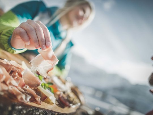 Skifahren in Ladurns Person greift nach dünnem Schinken auf einem Holzbrett im Freien