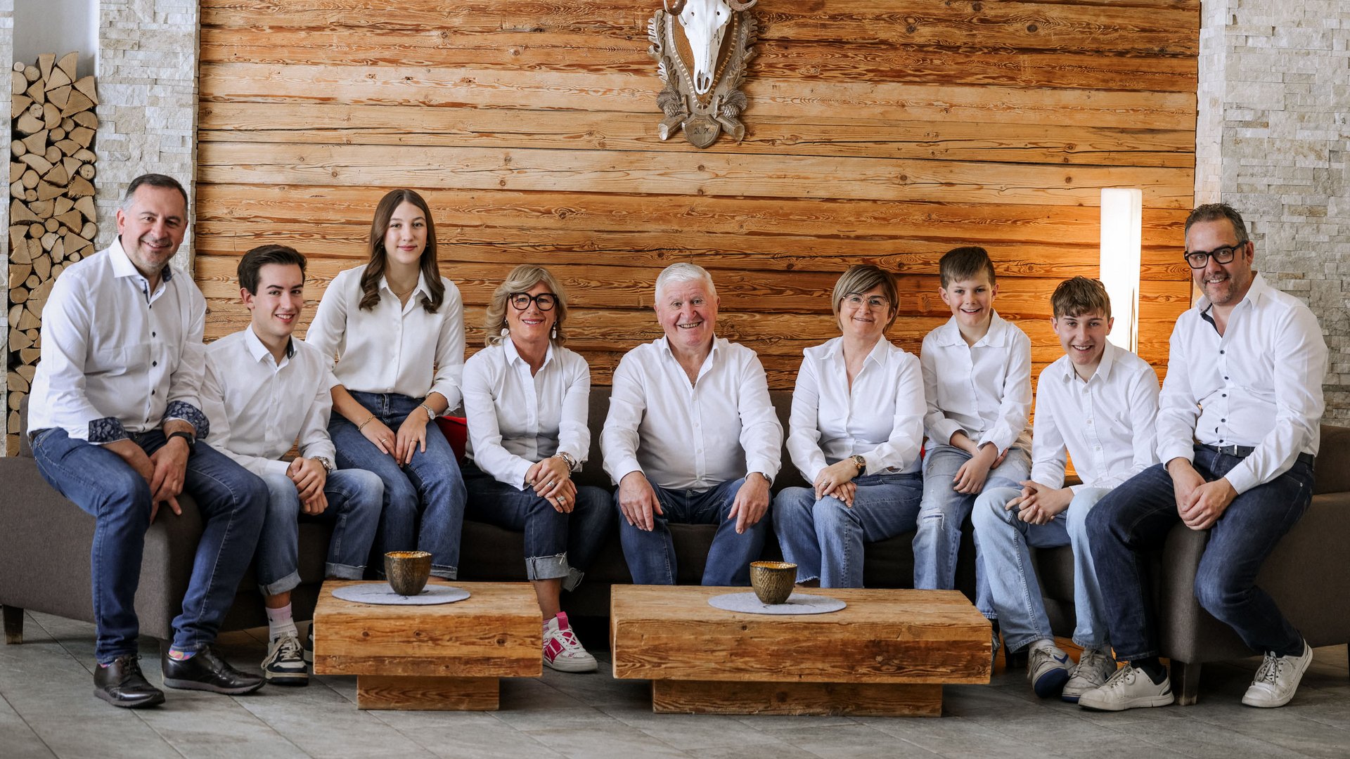 Family hotel in South Tyrol: Hotel Panorama Large family in white shirts sitting on sofa in front of wooden wall with deer skull