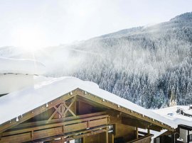 Familienhotel in Südtirol: Hotel Panorama Schneebedeckte Holzhütte vor verschneitem Wald und Bergen im Sonnenlicht