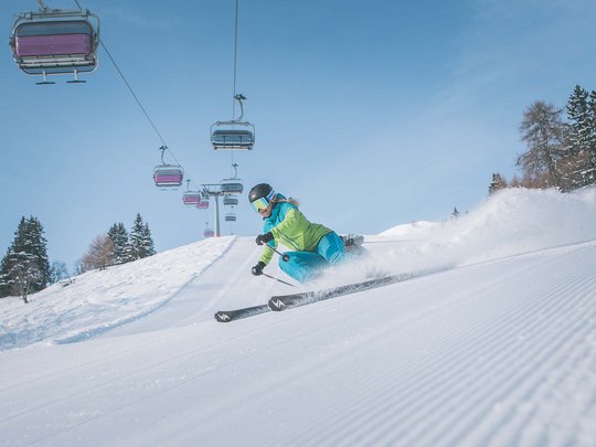 Skifahren in Ladurns Skifahrer fährt auf präparierter Piste unter Sessellift bei klarem Himmel