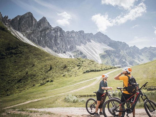 Lo sport a Colle Isarco vi coinvolgerà Due ciclisti con caschi davanti a montagne e valle verde invitanti per escursioni