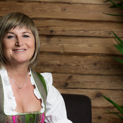 Familienhotel in Südtirol: Hotel Panorama Frau in traditionellem Dirndl vor Holzwand, freundlich lächelnd