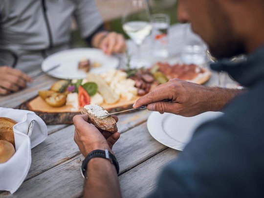 Aktivhotel Panorama: Wandern Person bestreicht Brot mit Frischkäse bei einem gemeinsamen Essen mit Käse und Aufschnitt