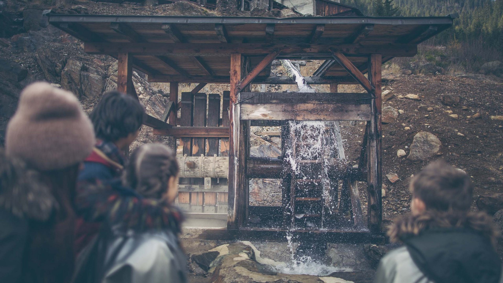 Dall’hotel a Colle Isarco a 3 stelle verso l’avventura Bambini osservano una ruota idraulica in funzione all'aperto in montagna