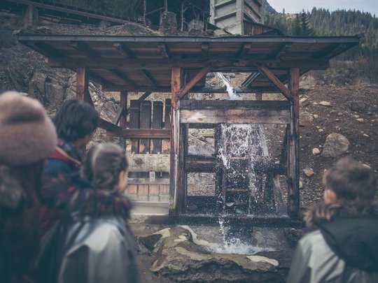 Hotel Panorama in Gossensass – Unterkunft zum Träumen Kinder beobachten ein funktionierendes Wasserrad im Freien in den Bergen