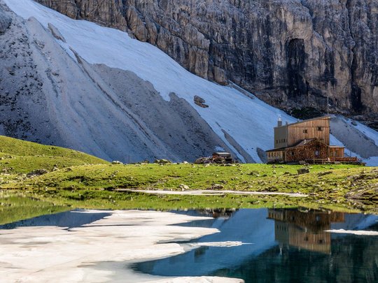 Aktivhotel in Südtirol: Sommererlebnisse Berghütte am See mit Eis, umgeben von grünen Wiesen und steilen Felsen
