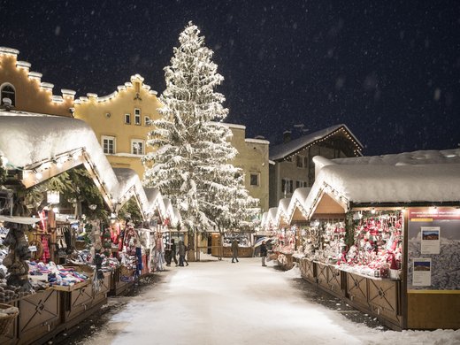 A Ladurns, c’è l’hotel perfetto per le vacanze invernali Mercatino di Natale invernale con albero decorato e bancarelle innevate di sera
