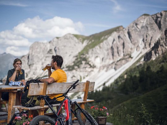 Pflerschtal: Unterkünfte furs Biken Zwei Radfahrer trinken Bier auf einer Bank vor Berglandschaft